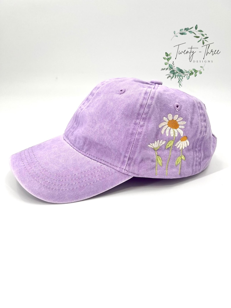 May include: A lavender baseball cap with embroidered white daisies. The cap has a slightly distressed look and is made of a soft, comfortable fabric.