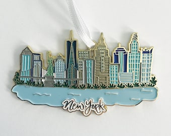 May include: Gold-colored metal ornament depicting the New York City skyline with blue and green accents. The ornament features the Statue of Liberty and the text "New York" in gold lettering.