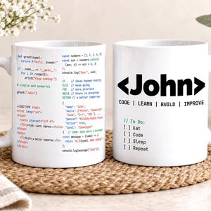 May include: Two white ceramic mugs featuring programming-themed designs. One mug displays colourful code snippets and HTML tags. The other mug features the name John in bold black text between angle brackets, with the text Code, Learn, Build, Improve.