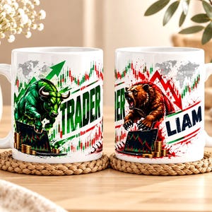 May include: Two white ceramic mugs featuring stock market graphics. One mug displays a green bull, upward trending charts, and the word TRADER. The other mug shows a brown bear, downward trending charts, and the name LIAM in bold dark blue letters.