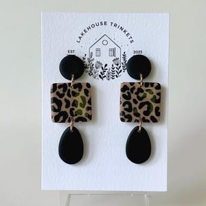 May include: A pair of black and brown leopard print dangle earrings with black teardrop-shaped dangles. The earrings are displayed on a white card with the text "Lakehouse Trinkets Est 2023".