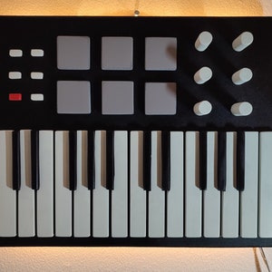 May include: A black MIDI keyboard with white keys and a 9-pad drum pad section. The keyboard has 4 white knobs on the right side.