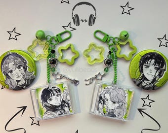 May include: Two keychains with green accents, star-shaped charms, and a small bell. Each keychain has a button with a portrait of a person wearing headphones and a small CD case with a portrait. The background has star and headphone graphics.