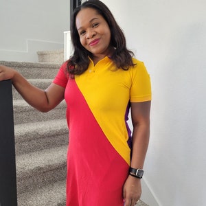 May include: A woman wearing a yellow, red, and purple color block dress with a collar and short sleeves. She is standing on a carpeted staircase.