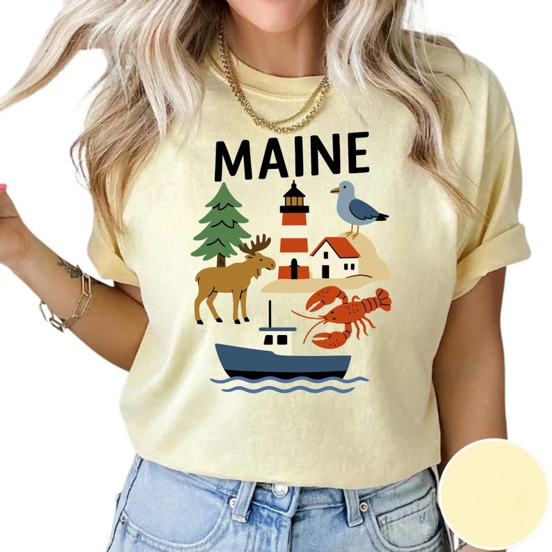 May include: A pale yellow t-shirt with the word "MAINE" in black. The shirt displays a graphic of a moose, lighthouse, seagull, lobster, pine tree, and boat.