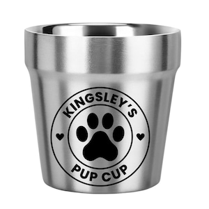 May include: A stainless steel "Pup Cup" with a black paw print design. The cup has a circular logo with the text "Kingsley's Pup Cup" and two small hearts. The cup is designed for pets.