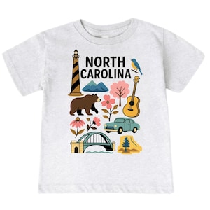 May include: A light gray t-shirt featuring a colorful graphic of North Carolina landmarks. The design includes a lighthouse, bear, mountains, flowers, a guitar, a car, a bridge, and the text "NORTH CAROLINA".