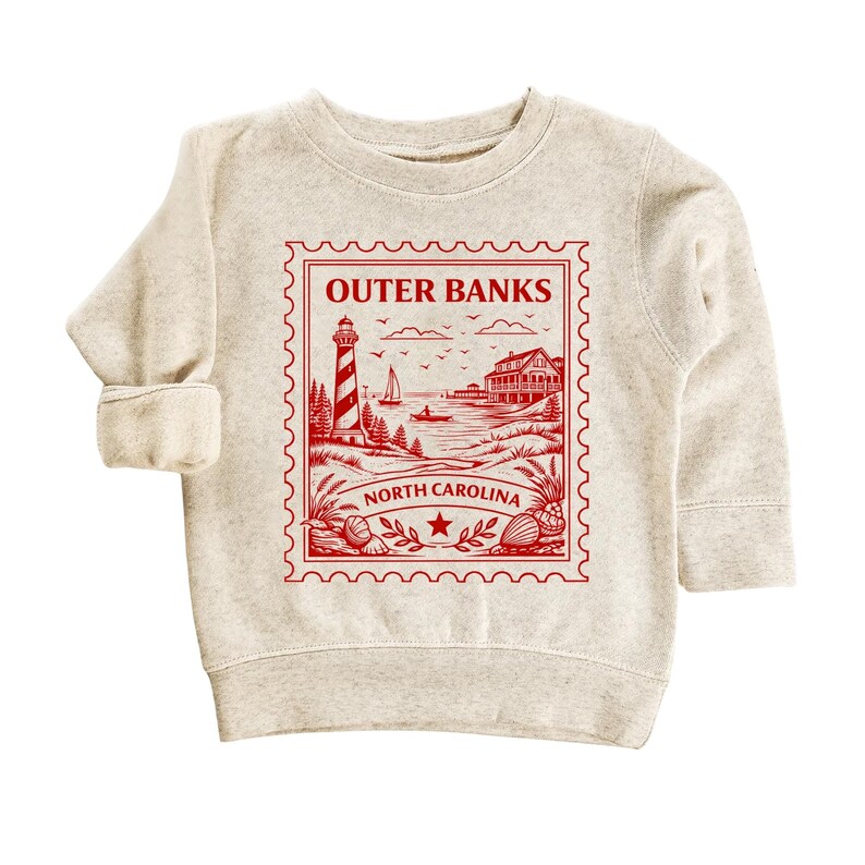 May include: A light beige sweatshirt featuring a red graphic of a lighthouse, beach scene, and the text "Outer Banks North Carolina" in a stamp design. The sweatshirt has long sleeves and a crew neck.