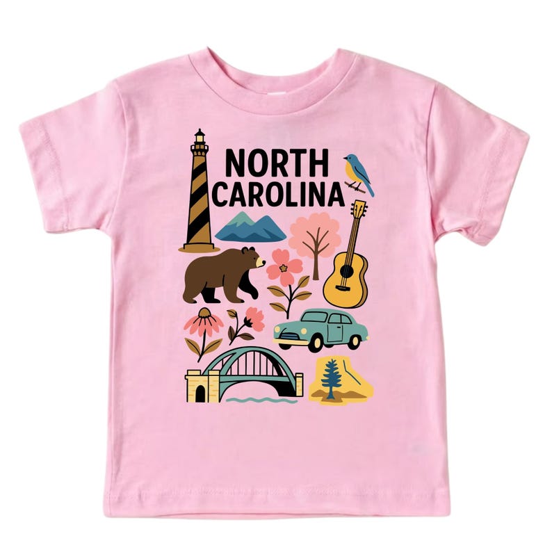 May include: Pink t-shirt featuring a colorful graphic design with the text "NORTH CAROLINA." The design includes a lighthouse, bear, mountains, flowers, a guitar, a car, a bridge, a bird, and a tree.