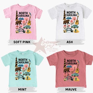 May include: Four short-sleeved t-shirts in soft pink, ash, mint, and mauve. Each shirt features a North Carolina design with a lighthouse, bear, guitar, car, bridge, and flowers. The shirts are labeled with their color.