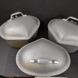 May include: Three silver heart-shaped aluminum cookware lids with textured surfaces and handles.