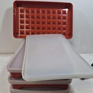 May include: Stack of red and gray plastic food storage containers with clear lids. The top container is open, revealing a textured interior. The containers are rectangular and appear to be collapsible for easy storage.