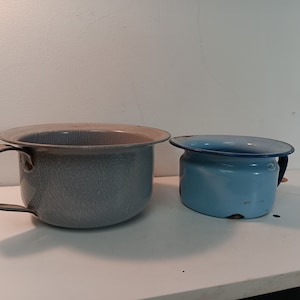 Puede incluir: Dos orinales de esmalte vintage, uno en azul claro y otro en gris con un acabado texturizado.