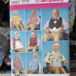 May include: A Simplicity sewing pattern envelope 2687 for adult bibs in one size. The front features illustrations of various bib styles, including floral, plaid, and solid designs, worn by individuals in different settings, with a barcode at the bottom.