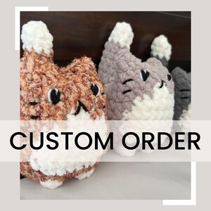 May include: Three crocheted cat plushies in different colors: orange, gray, and black. The plushies have white fur accents and embroidered facial features. The image text reads "CUSTOM ORDER".