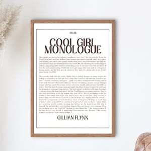 May include: A black and white print featuring the text "Cool Girl Monologue" and a quote by Gillian Flynn. The print is framed in a light brown wood frame and is hanging on a white wall.