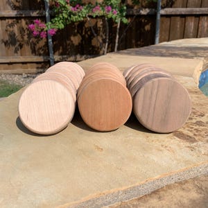 May include: A collection of round wooden coasters in varying shades of light, medium, and dark brown. The coasters are arranged in neat stacks, showcasing the natural wood grain. These coasters are perfect for protecting surfaces from drink rings.