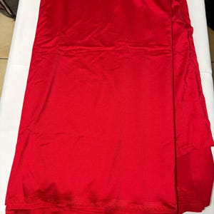 May include: A length of vibrant red fabric with a smooth, satin-like finish. The material is folded in layers, displaying a consistent, solid red color throughout. The edges show a subtle, fine-ribbed texture along the hem of the textile.