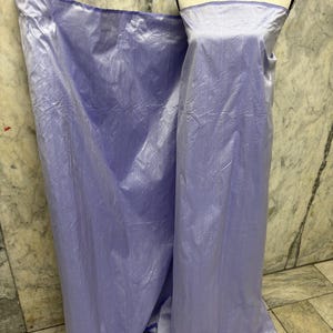 May include: A light purple, strapless dress on a mannequin, with a matching fabric draped to the side. The dress has a subtle sheen and appears to be made of a lightweight material. The background is a marble-like wall.
