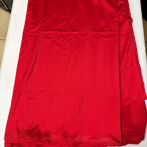 May include: A length of solid red fabric with a smooth, slightly reflective surface texture. The material is folded in layers, showing a consistent vibrant red color throughout the entire piece. The edges appear finished with a subtle horizontal ribbed pattern.