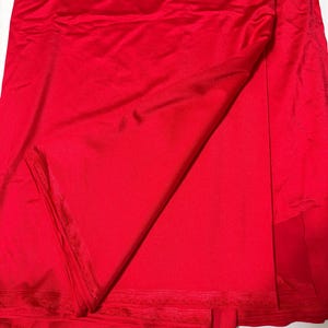 May include: A vibrant red fabric with a smooth, slightly reflective surface. The material is folded over itself, creating soft drapes and shadows that highlight the consistent, solid red color and the fine, woven texture of the textile edges.