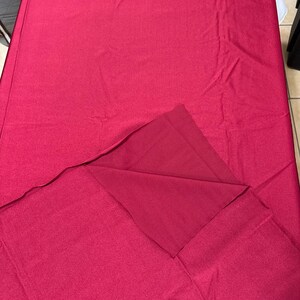 May include: A rectangular tablecloth in a solid deep magenta color. The fabric has a smooth, matte texture and is draped over a surface, with one corner folded back to reveal the underside of the same solid magenta material.