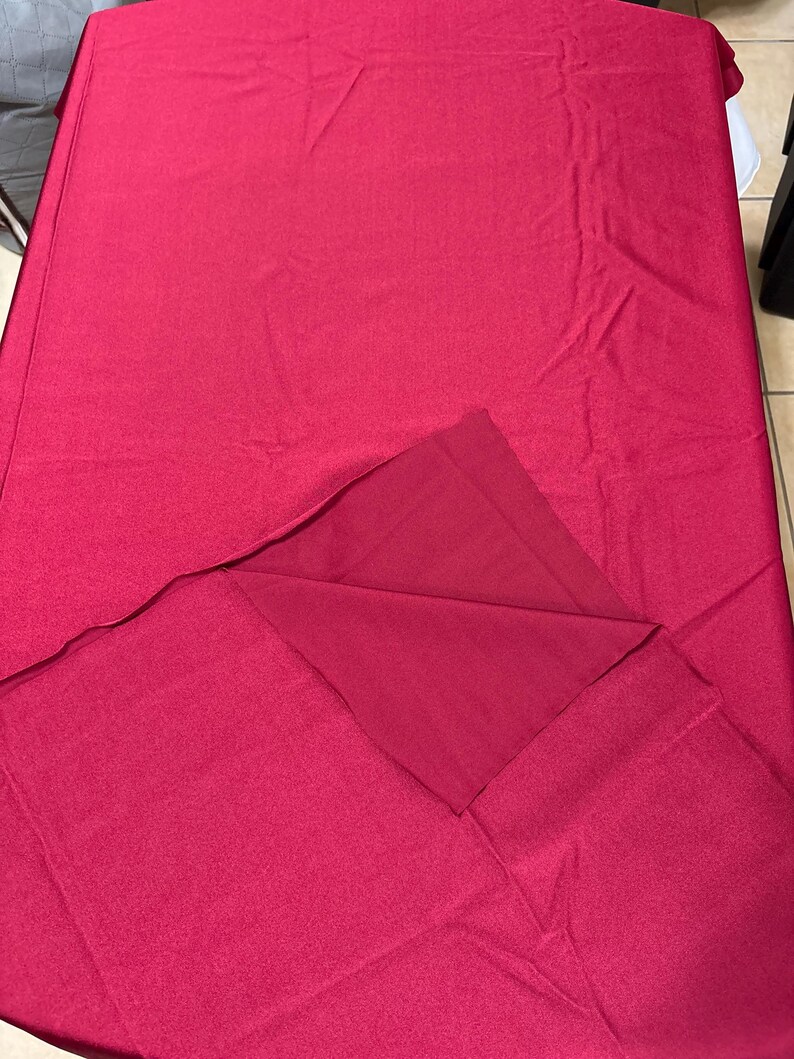 May include: A rectangular tablecloth in a solid deep magenta color. The fabric has a smooth, matte texture and is draped over a surface, with one corner folded back to reveal the underside of the same solid magenta material.