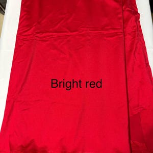May include: A length of bright red fabric with a smooth, slightly reflective surface. The material is folded, creating subtle vertical lines and shadows across the vibrant red surface. The text "Bright red" is printed in black in the center.