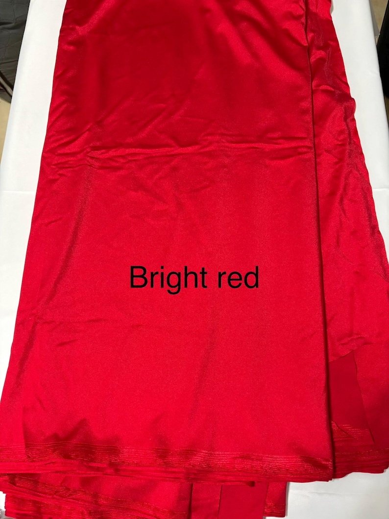 May include: A length of bright red fabric with a smooth, slightly reflective surface. The material is folded, creating subtle vertical lines and shadows across the vibrant red surface. The text "Bright red" is printed in black in the center.