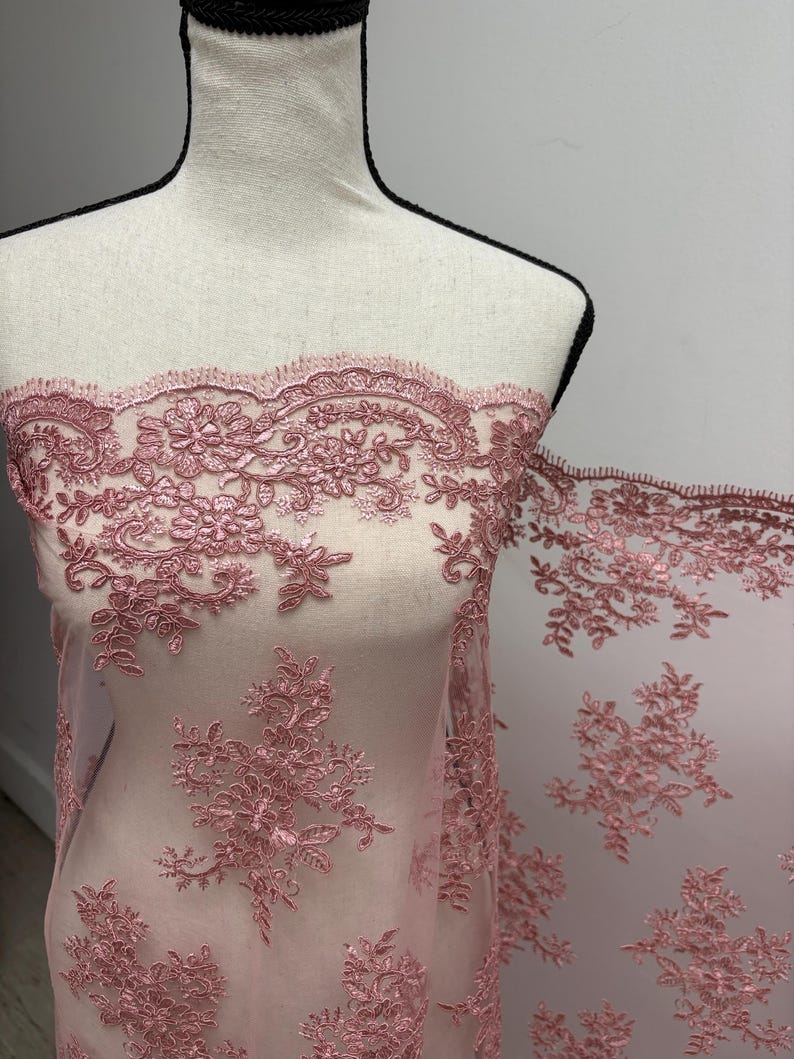 K&ouml;nnte beinhalten: Staubrosa Spitzenstoff mit floraler und Blattstickerei. Die zarte Spitze wird auf einer Schaufensterpuppe pr&auml;sentiert, die die komplizierten Details und die Textur zeigt. Ideal f&uuml;r Brautmode, Kleider oder andere besondere Anl&auml;sse.