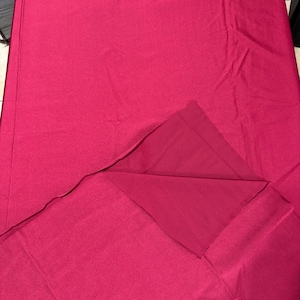 May include: A solid deep magenta fabric piece with a smooth, matte texture. The material is folded over at the bottom right corner, revealing a slightly darker shade of the same magenta color on the underside of the fabric layer.