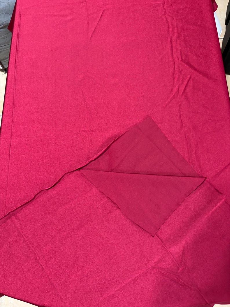 May include: A solid deep magenta fabric piece with a smooth, matte texture. The material is folded over at the bottom right corner, revealing a slightly darker shade of the same magenta color on the underside of the fabric layer.