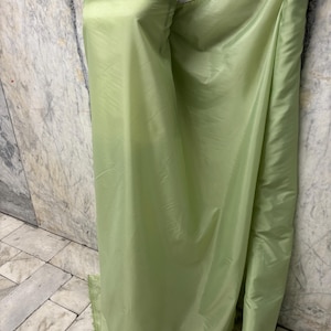 May include: A bolt of light green fabric is draped over a mannequin. The fabric has a shiny, smooth texture and appears to be lightweight. The fabric is a solid color and is rolled up on the right side of the image.