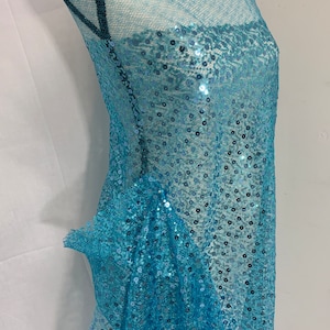 May include: Turquoise blue sequined fabric with a sheer mesh backing. The sequins are small and evenly distributed throughout the fabric.