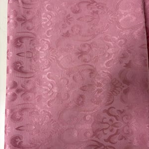 May include: A folded piece of pink fabric with a repeating floral pattern. The fabric has a subtle sheen, and the design is slightly raised, creating a textured effect. The overall look is elegant and suitable for various textile projects.