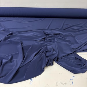 May include: A bolt of solid navy blue fabric featuring a smooth, matte texture. The material is draped in soft folds across a white surface, with handwritten text visible on the surface reading 13 INCH and 3/4 YD.