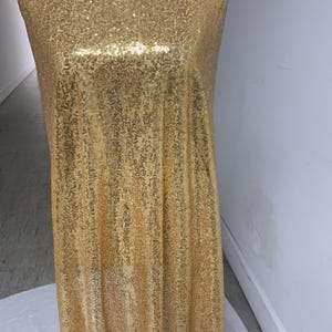 Könnte beinhalten: Goldfarbener Paillettenstoff mit glatter, glänzender Oberfläche. Der Stoff ist über eine Schaufensterpuppe drapiert.