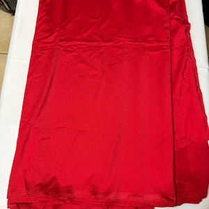 May include: A vibrant red fabric with a smooth, slightly reflective surface texture. The material is folded in layers, displaying a consistent solid color throughout. The edges show a subtle horizontal ribbed pattern along the hemline of the textile.