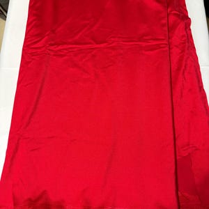May include: A vibrant red fabric with a smooth, slightly reflective surface texture. The material is folded in layers, displaying a consistent solid crimson color throughout. The bottom edge features a subtle horizontal ribbed pattern detail.