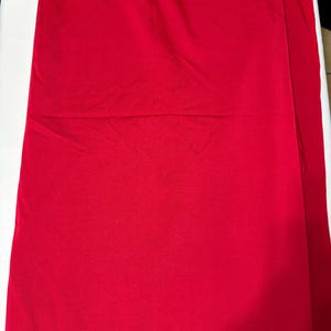 May include: A solid, vibrant red fabric with a smooth, matte texture. The material is draped in soft, gentle folds, creating subtle shadows and highlights across the surface. The color is consistent throughout, showing a deep, saturated red hue.