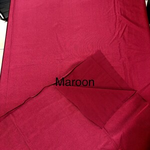 May include: A rectangular maroon fabric textile with a smooth, matte finish. The material is folded over at one corner, revealing a slightly darker shade of the same maroon color on the underside. The word Maroon is printed in black text.