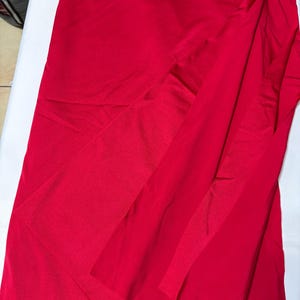 May include: A vibrant red skirt featuring a smooth, satin-like finish and a wrap-style design. The garment displays a layered front panel that creates a diagonal overlap, resulting in a clean, fluid silhouette with soft folds throughout the fabric.
