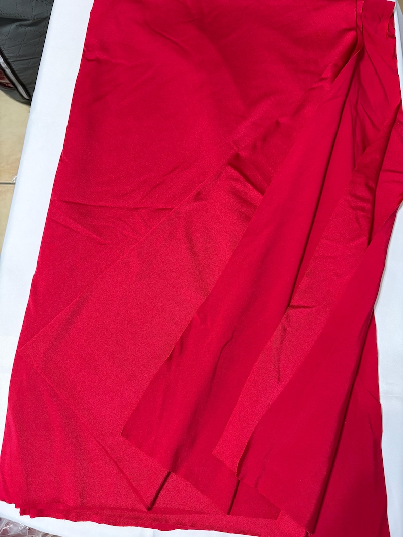 May include: A vibrant red skirt featuring a smooth, satin-like finish and a wrap-style design. The garment displays a layered front panel that creates a diagonal overlap, resulting in a clean, fluid silhouette with soft folds throughout the fabric.