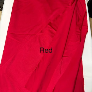 May include: A solid, vibrant red fabric with a smooth, slightly reflective surface texture. The material is draped in soft, vertical folds, creating natural shadows and highlights across the surface. The word Red is printed in black text.
