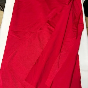 May include: A vibrant red fabric with a smooth, slightly reflective surface. The material is draped in a way that creates soft folds and layers, showcasing the consistent, solid red color throughout the entire piece of textile.
