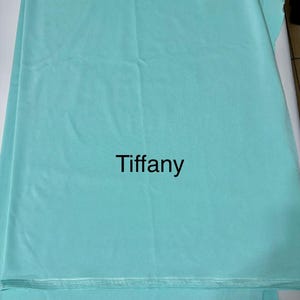 May include: A solid light turquoise fabric featuring the word Tiffany printed in black in the center. The material has a smooth, matte texture with visible horizontal folds and a finished edge at the bottom, displaying a consistent color throughout.