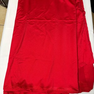 May include: A solid, vibrant red fabric with a smooth, slightly reflective surface texture. The material is folded in layers, showing a consistent, deep crimson color throughout the entire piece of textile, which appears to be a single, continuous length.