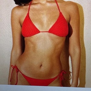 May include: A bright red bikini set featuring a textured, ribbed fabric. The top is a classic triangle style with thin halter neck straps, and the bottom is a low-rise piece with adjustable side ties that knot at the hips for a secure fit.