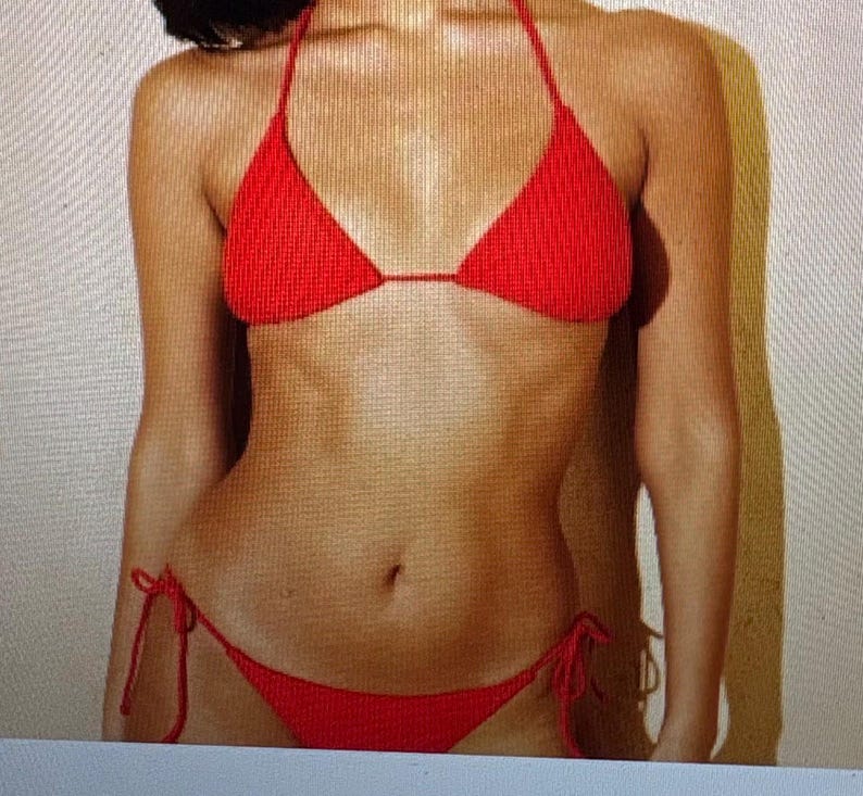 May include: A bright red bikini set featuring a textured, ribbed fabric. The top is a classic triangle style with thin halter neck straps, and the bottom is a low-rise piece with adjustable side ties that knot at the hips for a secure fit.