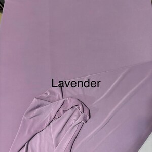 May include: A solid lavender colored fabric with a smooth, matte texture. The material is draped to show its flexibility and soft folds. The word Lavender is printed in black text in the center of the image, indicating the color of the textile.
